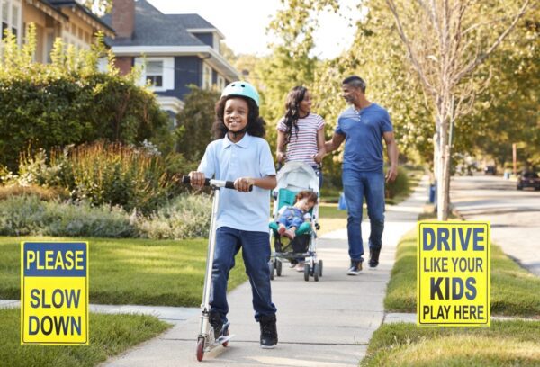 A picture of a couple, a toddler in a stroller, and a kid on a scooter in an area with two traffic safety signs